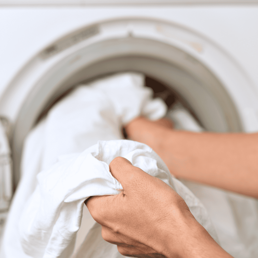 Hands Holding Sheets With a Washing Machine in the Background